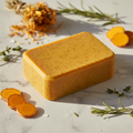 Turmeric Herbal Soap bar on white marble with turmeric root and dried herbs